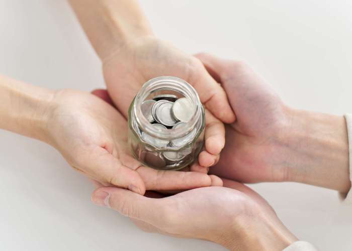 Hands of a man and woman carrying a jar containing coins
